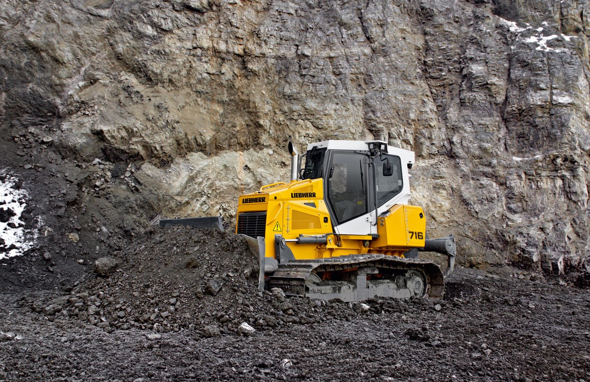 A Liebherr crawler tractor pushing a rock pile along a cliff wall in a quarry