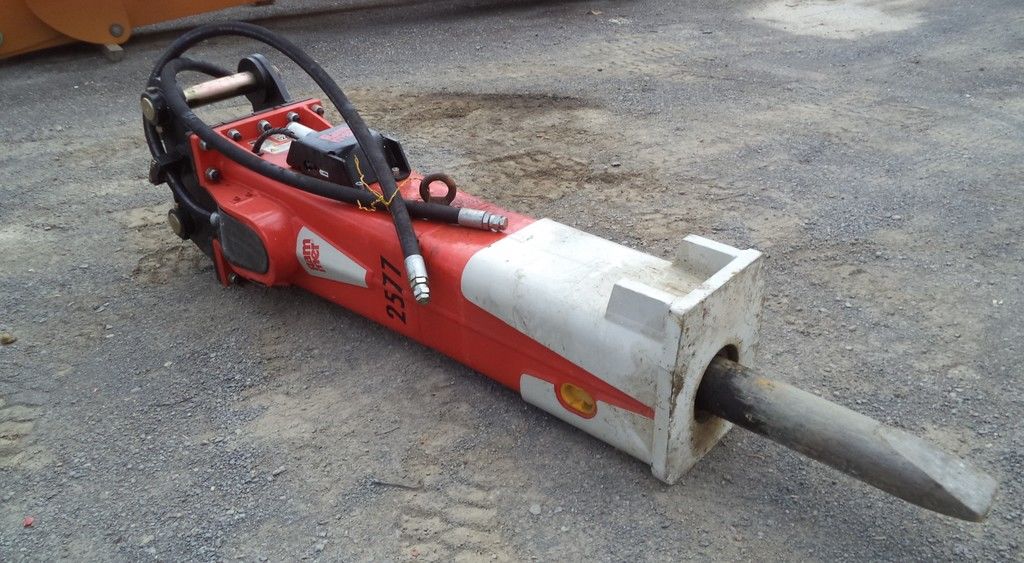 Red 2019 Rammer 2577 hydraulic breaker set down on a gravel surface.